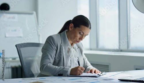 A professional businesswoman writing at her desk in an office showing focus and productivity