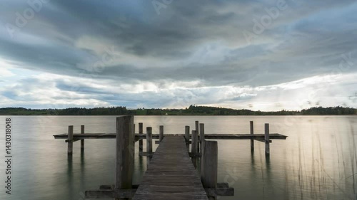Wallpaper Mural Sunset on a lake, on a jetty, under cloudy skies and stormy clouds. The sun's rays pierce the clouds. In the background, you can see the hilly landscape, and it's springtime. Torontodigital.ca