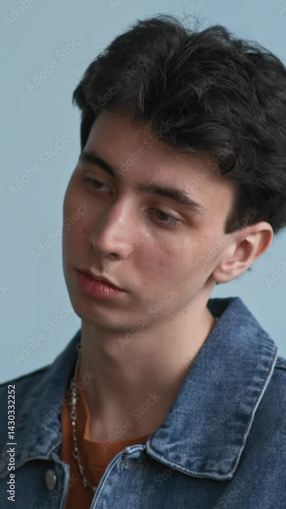 Vertical medium close up shot of pensive Caucasian teenage boy in denim jacket sitting in classroom immersed in his thoughts while unrecognizable teacher going back and forth holding clipboard Vertical medium close up shot of pensive Caucasian teenage boy in denim jacket sitting in classroom immersed in his thoughts while unrecognizable teacher going back and forth holding clipboard