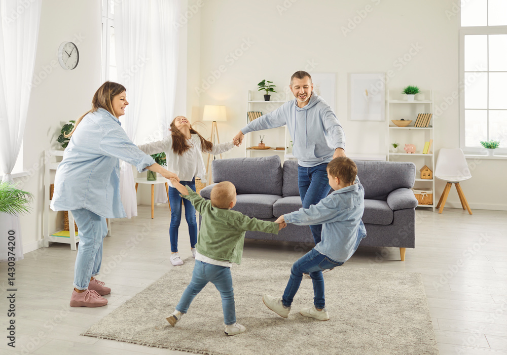 Happy large family holding hands and dancing in circle in spacious living room. Smiling parents and three children enjoying playful activity together, having fun and dancing in round dance at home.