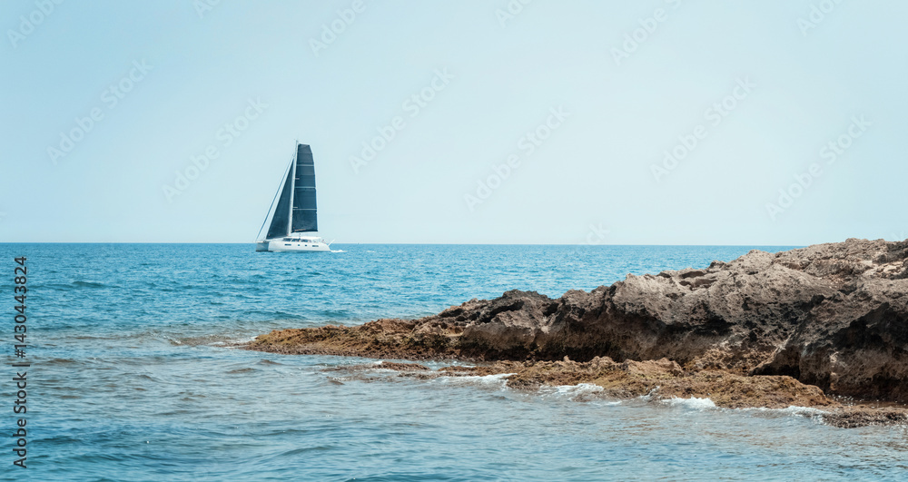 Seascape with sailboat behind island under blue cloudless sky. Nautical spirit and summer holidays