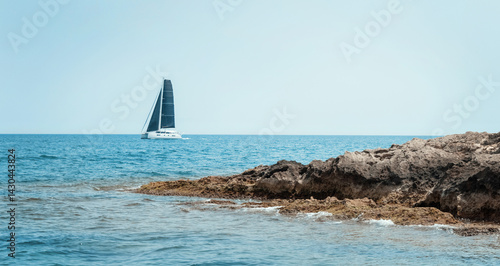 Obraz na płótnie Seascape with sailboat behind island under blue cloudless sky. Nautical spirit and summer holidays w salonie