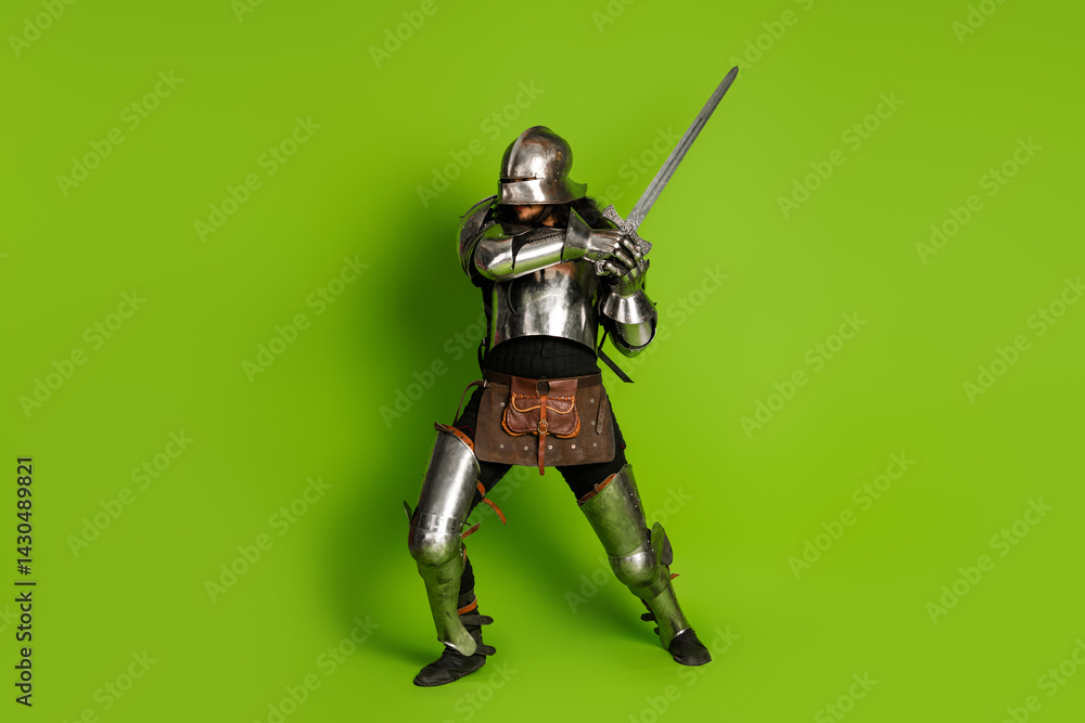 Young man in medieval armor with sword against green background showing knight history and bravery Young man in medieval armor with sword against green background showing knight history and bravery