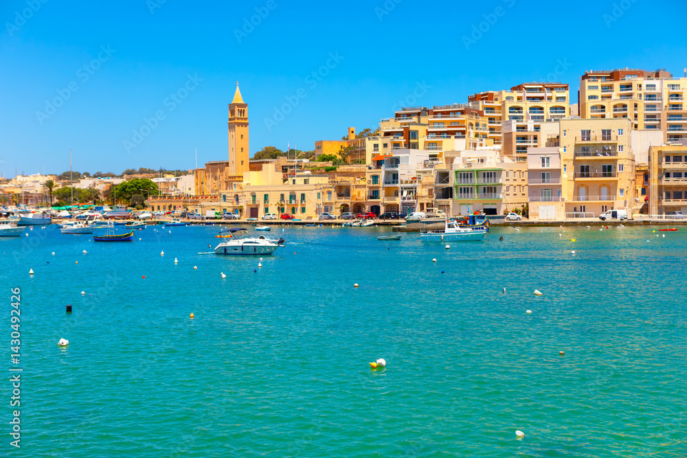 Colorful waterfront view of Marsaskala, Malta. Boats gently float in turquoise waters against a backdrop of pastel buildings and a tall church tower under a clear blue sky. Perfect Mediterranean vibe.