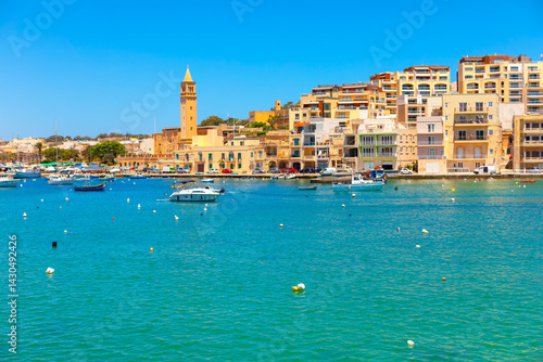 Obraz na płótnie Colorful waterfront view of Marsaskala, Malta. Boats gently float in turquoise waters against a backdrop of pastel buildings and a tall church tower under a clear blue sky. Perfect Mediterranean vibe. w salonie