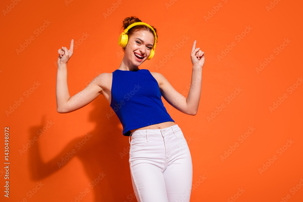 Joyful young woman wearing a vibrant outfit and headphones enjoying music against a bright orange background