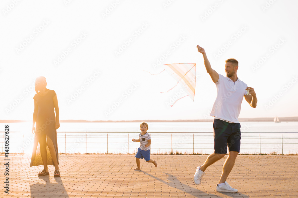 Family Running Together With Flying Kite Outdoors