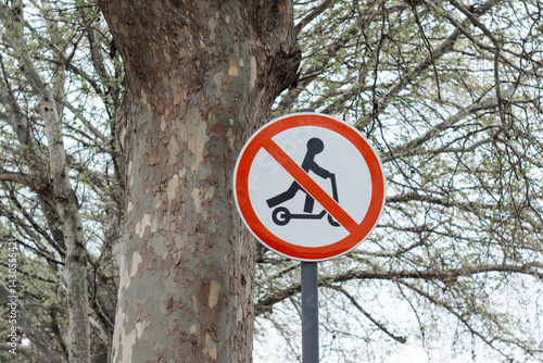 Sign in park with crossed out electric scooter. Ban on riding scooter in public place on street of modern city