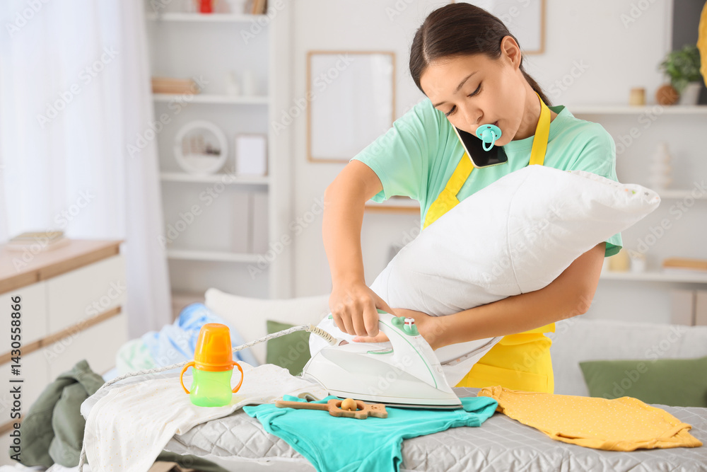 Overwhelmed Asian mother with baby ironing clothes while talking by phone at home. Multitasking concept Overwhelmed Asian mother with baby ironing clothes while talking by phone at home. Multitasking concept