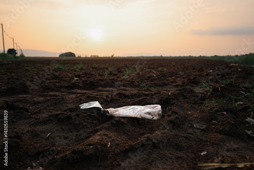 A crumpled plastic bottle lies abandoned on a field at sunset, symbolizing pollution and human disregard for the environment.
