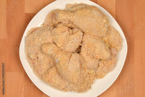 Obraz na płótnie Several pieces of breaded raw chicken, including drumsticks and cutlets, are arranged on a white plate ready for cooking w salonie