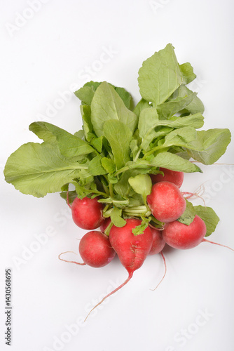 Obraz na płótnie A bunch of fresh red radishes with vibrant green leaves is presented on a plain light gray surface from a slightly elevated perspective w salonie