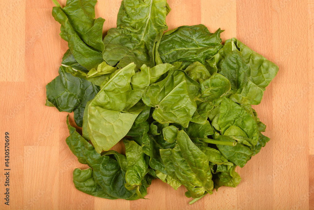 A pile of fresh, vibrant green spinach leaves is scattered on a light wooden surface, captured from a top-down perspective