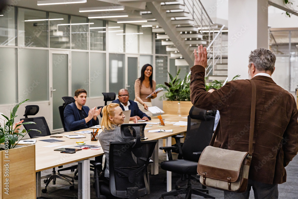 A White elderly employee bids farewell to his diverse coworkers by waving goodbye after a meeting in an office, as they smile at him. A concept of respect and positive relationships among colleagues. A White elderly employee bids farewell to his diverse coworkers by waving goodbye after a meeting in an office, as they smile at him. A concept of respect and positive relationships among colleagues.