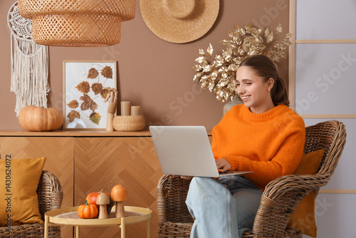 Young woman using laptop in armchair at home on autumn day