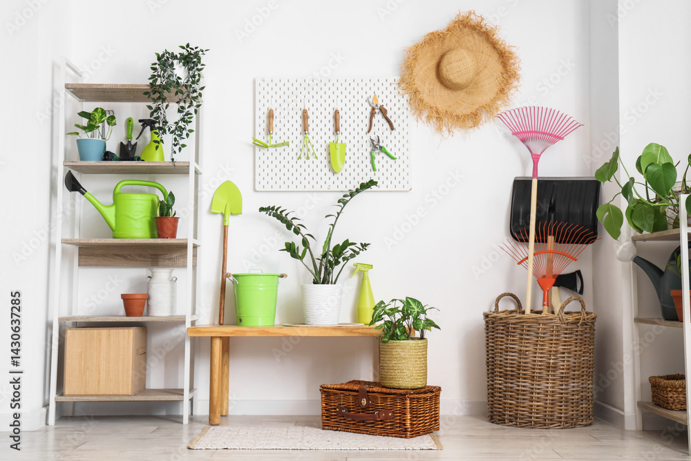 Fototapeta premium Workplace with pegboard, gardening tools and plants near white wall in barn