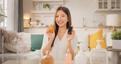 POV webcam view of Asian woman beauty influencer, content creator smiling while presenting skincare products to camera at home. vlog self care product review. Gen Z lifestyle social media trends.