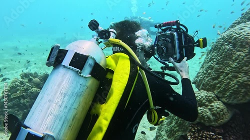 Man with oxygen balloon shoots coral colony growing on old rock undersea. Man biologist records exotic fauna of ocean biome diving in clear water. Scientific research