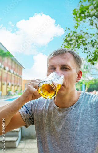 Close up of man drinking beer from glass at the open air near the pool. Alcohol and leisure concept.