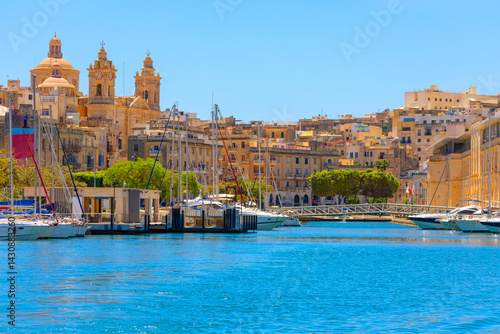 Obraz na płótnie Birgu fortified city on the south side of the Grand Harbour of Malta. Vibrant coastal cityscape features a waterfront with numerous boats and yachts docked along harbor, framed by clear blue water w salonie