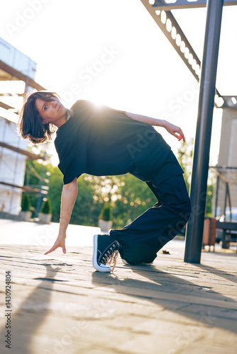 Young dancer performs dynamic pose outdoors during golden hour in urban environment