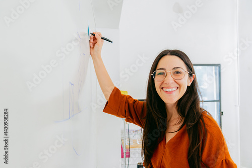 Young latina woman, writes on a white board in the office and smiles looking at the camera