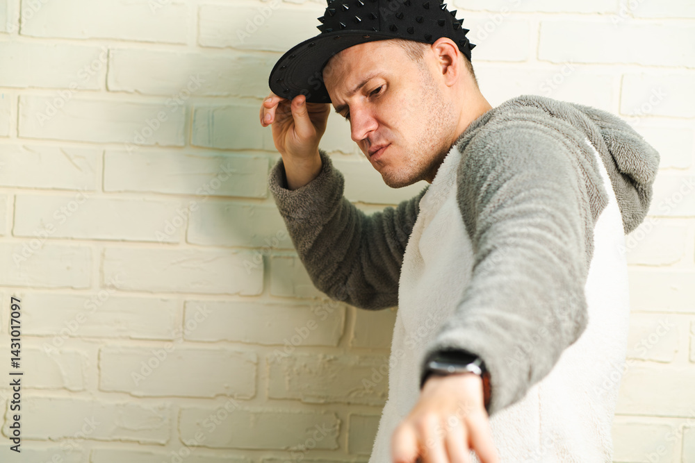 A man wearing a black cap and a gray sweater is captured in motion, dancing gracefully with fluid movements. His outfit contrasts against the background as he enjoys his dance. A man wearing a black cap and a gray sweater is captured in motion, dancing gracefully with fluid movements. His outfit contrasts against the background as he enjoys his dance.