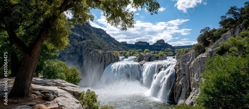 A cascade of water rushes down the rocky cliff face, surrounded by green forest