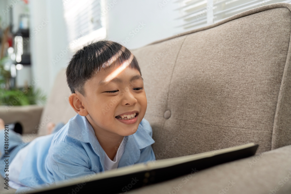 © Natee Meepian - Back to School and Digital Learning. A boy happily engaged with a tablet, embracing modern education methods.