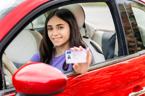 Young woman showing driving license while sitting in a red car