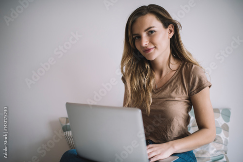 Portrait of millennial female freelancer with modern netbook doing distance jog using wireless internet connection for PC projecting, skilled woman with laptop computer looking at camera indoors
