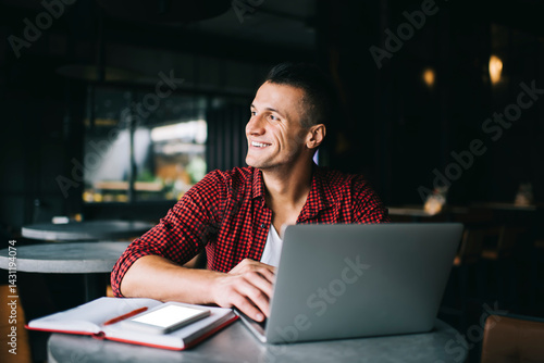 Cheerful man working on laptop while sitting at table in cafe