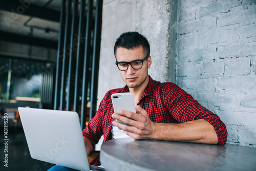 Focused man with smartphone browsing laptop