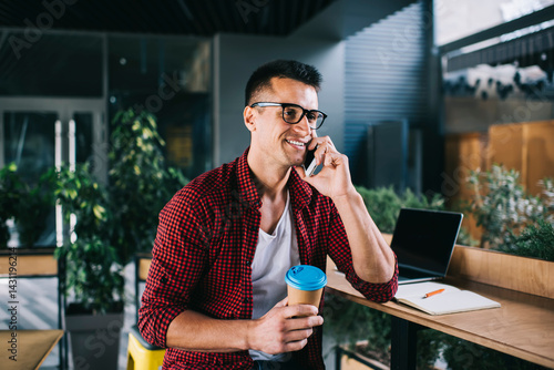 Smiling man with takeaway beverage talking on smartphone