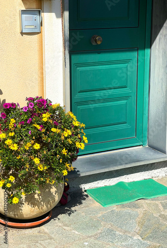 Old street in Italian countryside near sea. Traditional building. Sun day. Entrance, door to house with red, yellow flowers in pots. Nature and garden. Seasons and nature. Background for design.