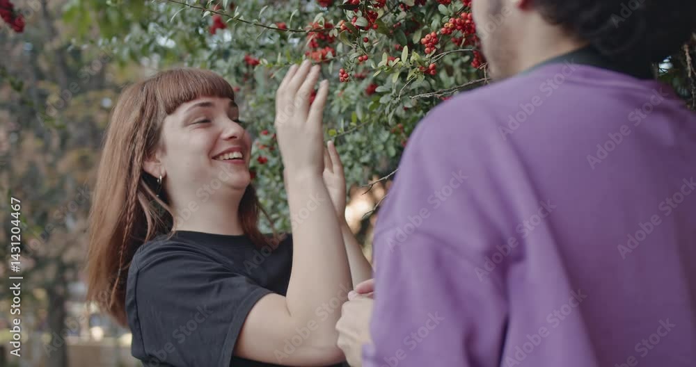 A young couple shares a playful moment in a park, examining berries on a tree and laughing together. A young couple shares a playful moment in a park, examining berries on a tree and laughing together.