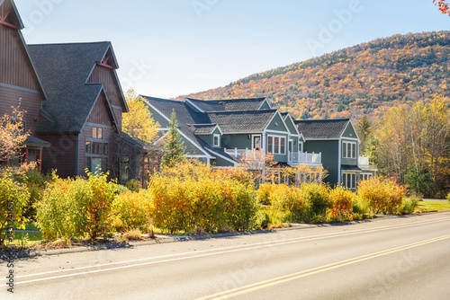 New luxury row houses along a road in a mountain village on a sunny autumn day. Forested mountains at the peak of fall foliage are in background.
