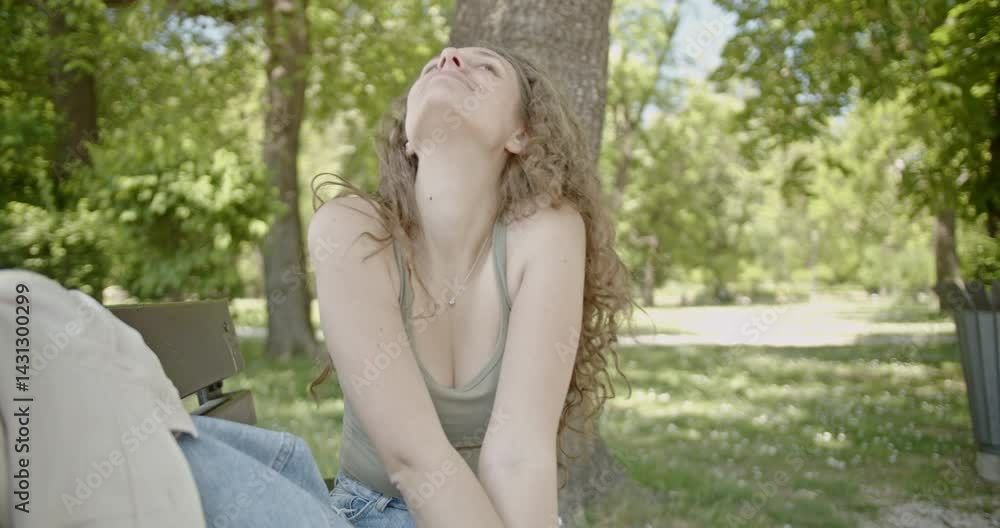 Young woman enjoying a sunny day in the park. She sits on a bench, breathes in the fresh air, smiles, and laughs. Young woman enjoying a sunny day in the park. She sits on a bench, breathes in the fresh air, smiles, and laughs.