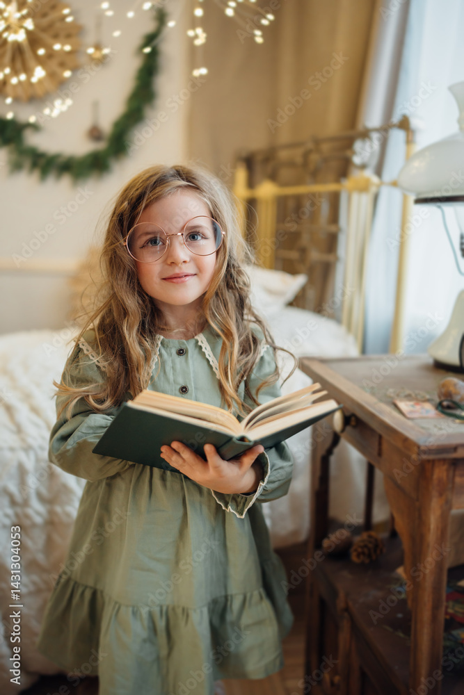 A beautiful little girl in a green dress and large round glasses with a book.