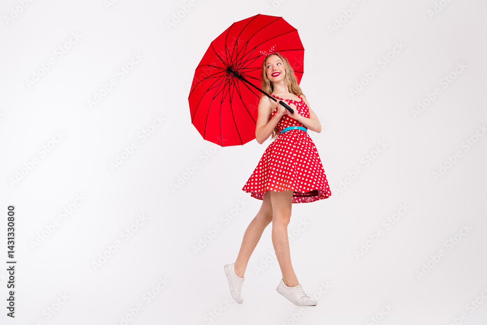 Fashionable young woman in retro polka dot dress holding a red umbrella in a stylish pose against a white background