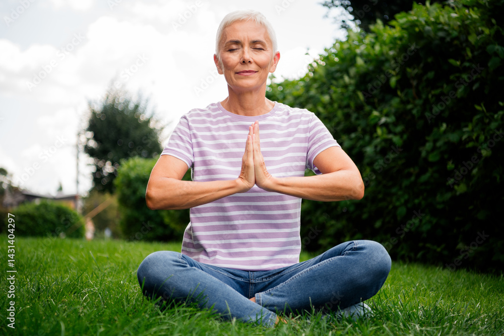 Obraz premium Mature woman practicing meditation outdoors under natural daylight in casual attire, enjoying a moment of peace and mindfulness