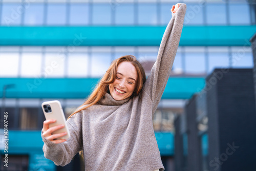 Obraz na płótnie Woman celebrating with joy outdoors while looking at her smartphone in an urban