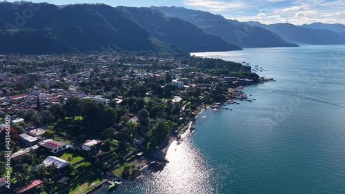 Beautiful cinematic aerial view os the Panajachel town surrounded by Toliman and Atitlan volcanoes, next to the Atitlan lake its piers and traditional fisher and tourist boats - Guatemala