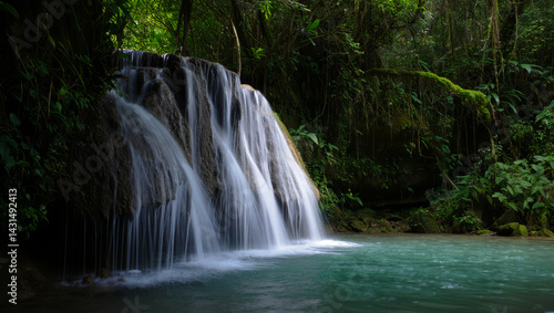 Serene long exposure wide shot of a multi-tiered waterfall cascading into a turquoise pool surrounded by lush green tropical rainforest jungle foliage
