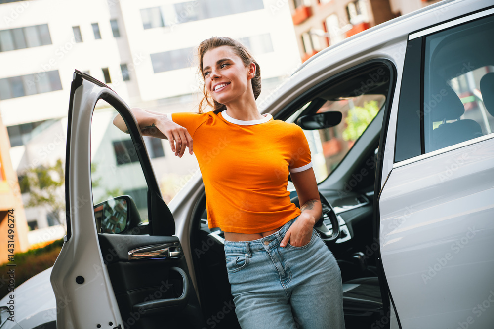 Young cheerful woman standing next to a car door in a vibrant urban setting during daylight, radiating confidence and charm