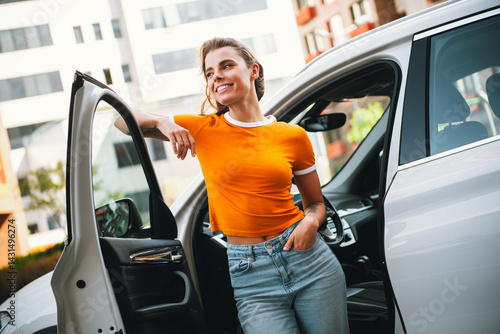 Obraz na płótnie Young cheerful woman standing next to a car door in a vibrant urban setting during daylight, radiating confidence and charm w salonie