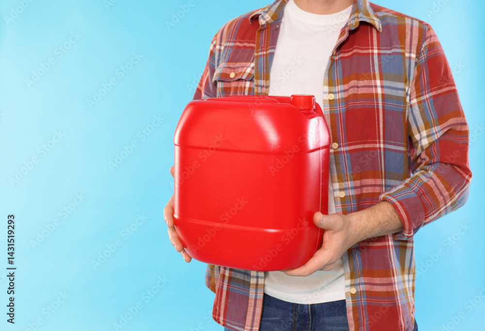 Fototapeta premium Man holding plastic canister on light blue background, closeup. Space for text