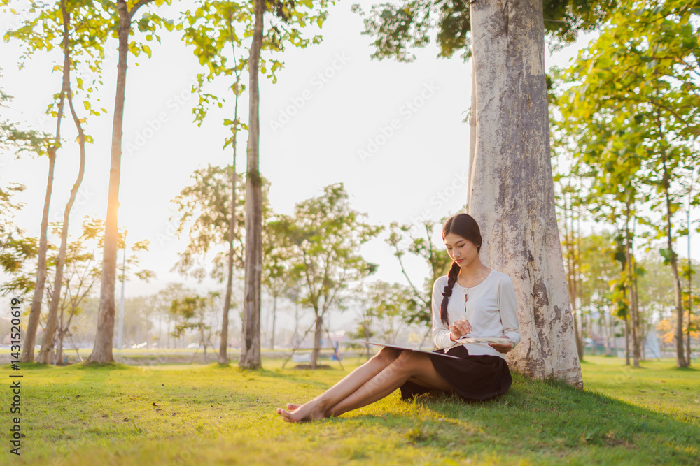 Bathed in warm golden light beneath a tree, a smiling female student immerses herself in her artwork, finding joy in the quiet beauty of the moment.