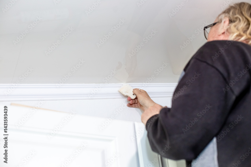 A man uses a rubber spatula to fill the joints on the ceiling after installing skirting boards. Home renovation A man uses a rubber spatula to fill the joints on the ceiling after installing skirting boards. Home renovation