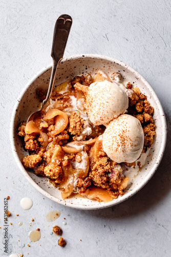 A bowl of apple crumble topped with two scoops of vanilla ice cream and a sprinkle of cinnamon.